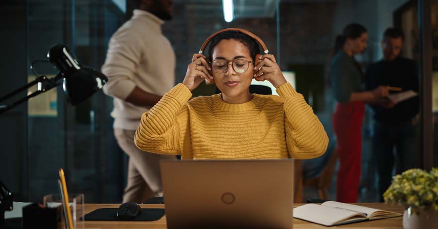 Woman putting on headphone in front of laptop at work