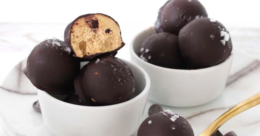 Cookie dough protein balls covered in chocolate, one ball cut open