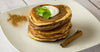Stack of pancakes on a white plate with cream on top and a cinnamon stick on the side